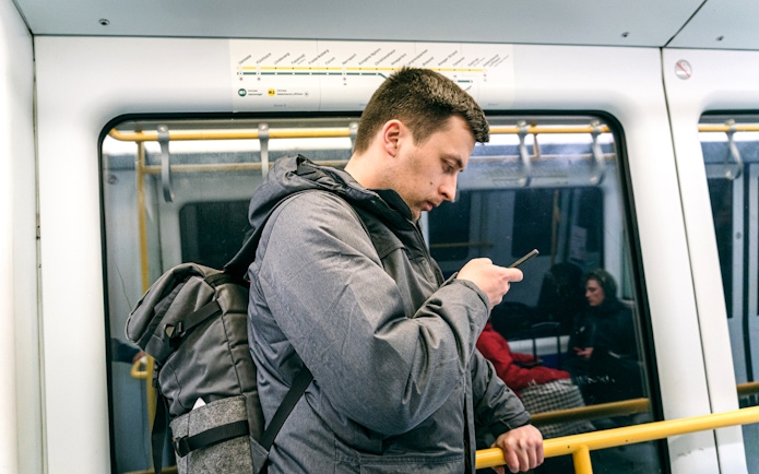 Man using phone on Copenhagen metro with city map above.