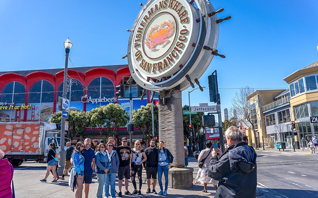 Tourist photographing group near Fisherman’s Wharf sign, San Francisco.