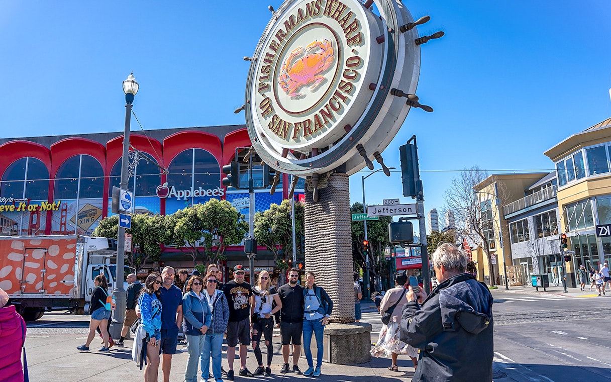 Tourist photographing group near Fisherman’s Wharf sign, San Francisco.