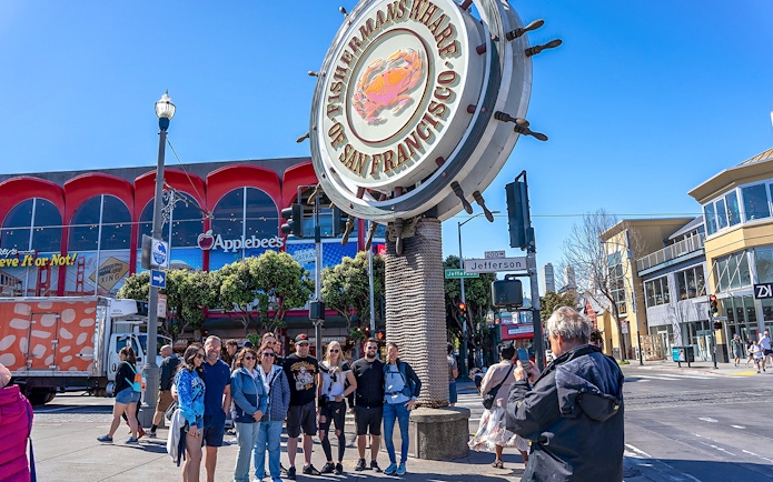 Tourist photographing group near Fisherman’s Wharf sign, San Francisco.