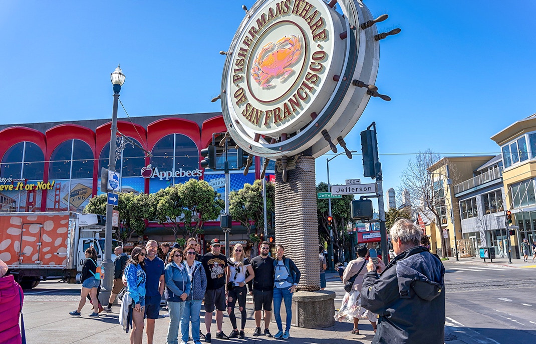 Tourist photographing group near Fisherman’s Wharf sign, San Francisco.