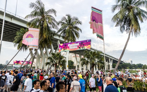 Crowd at Coconut Grove during Singapore F1 event under palm trees and bridge.