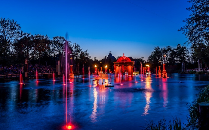 Evening fountain show with red lights at Puy du Fou, France.