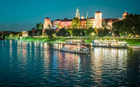 Night cruise on Vistula River with Wawel Royal Castle illuminated in the background, Krakow.