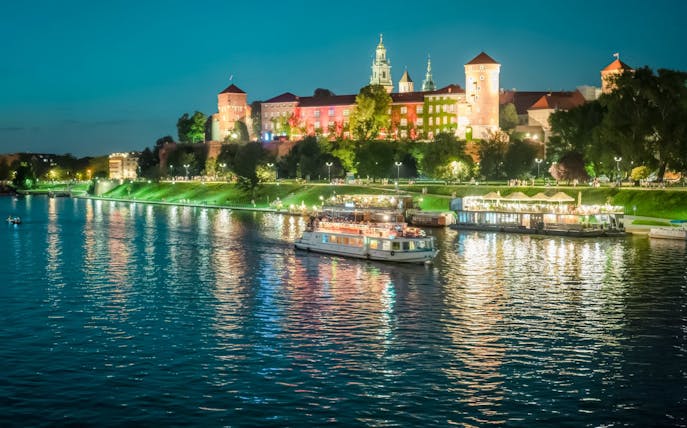 Night cruise on Vistula River with Wawel Royal Castle illuminated in the background, Krakow.