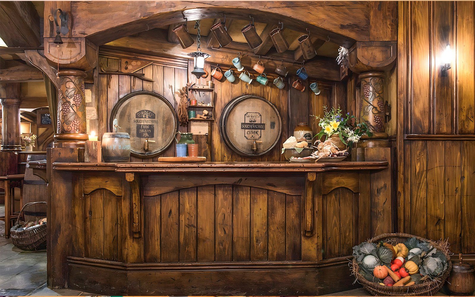 Rustic bar at Green Dragon Inn, Hobbiton Movie Set, with wooden barrels, mugs, and fresh produce.