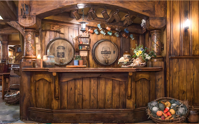 Rustic bar at Green Dragon Inn, Hobbiton Movie Set, with wooden barrels, mugs, and fresh produce.