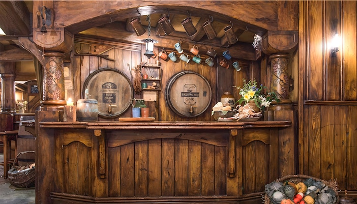 Rustic bar at Green Dragon Inn, Hobbiton Movie Set, with wooden barrels, mugs, and fresh produce.