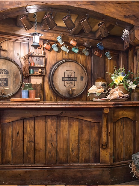 Rustic bar at Green Dragon Inn, Hobbiton Movie Set, with wooden barrels, mugs, and fresh produce.