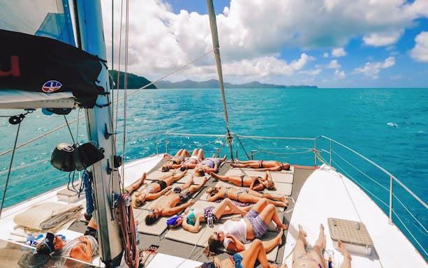 Tourists sunbathing on a sailboat deck in the Whitsundays.