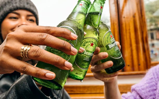 Guests toasting with Heineken bottles on Amsterdam canal cruise.