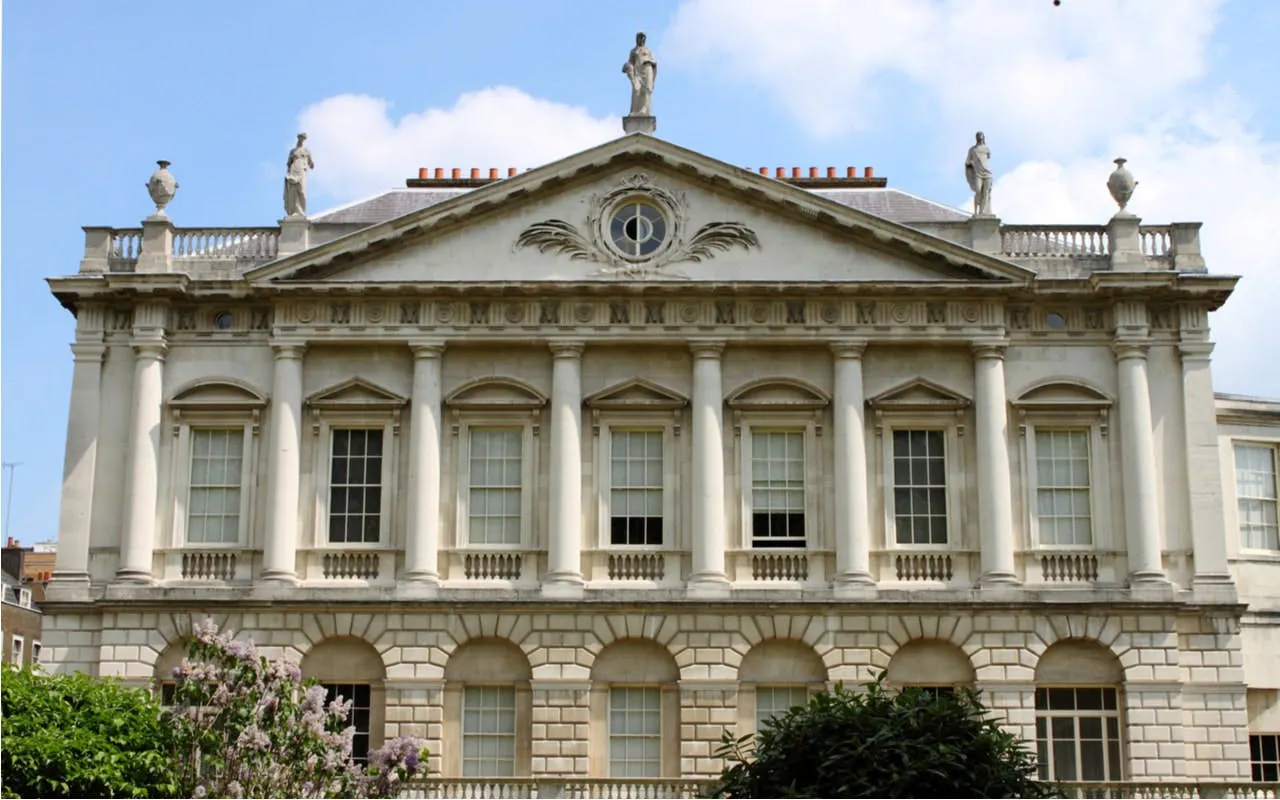 Facade of Spencer House in London, featuring neoclassical architecture with statues and columns.