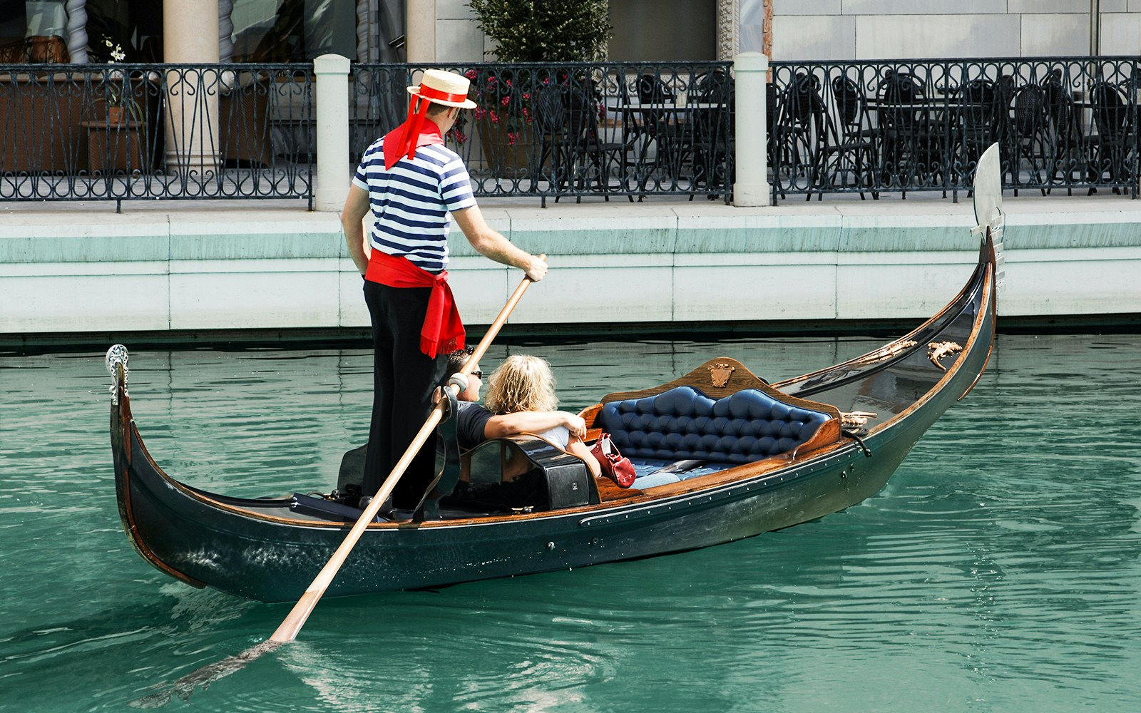 Gondolier steering a gondola with a passenger on a canal in Venice.