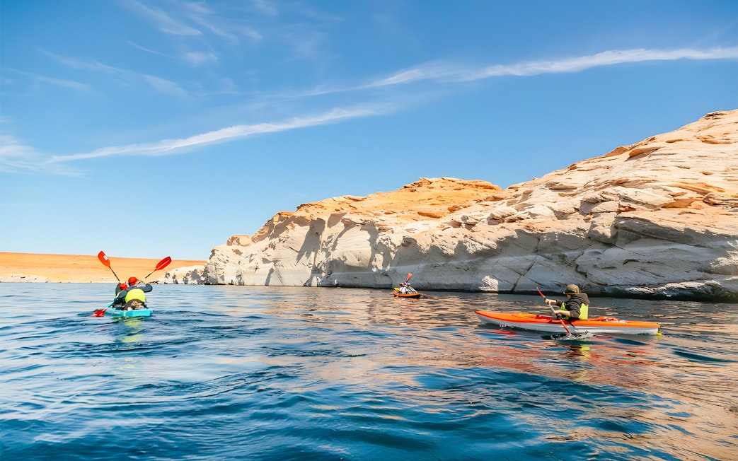 Kayakers paddling on Lake Powell near Antelope Canyon's sandstone cliffs.