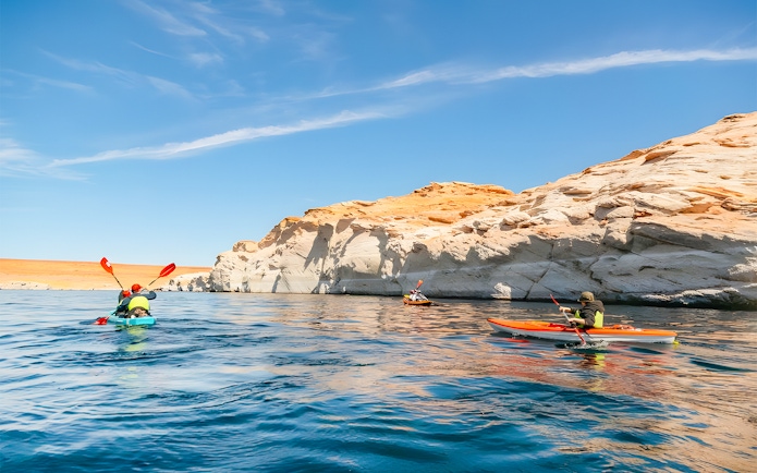 Kayakers paddling on Lake Powell near Antelope Canyon's sandstone cliffs.