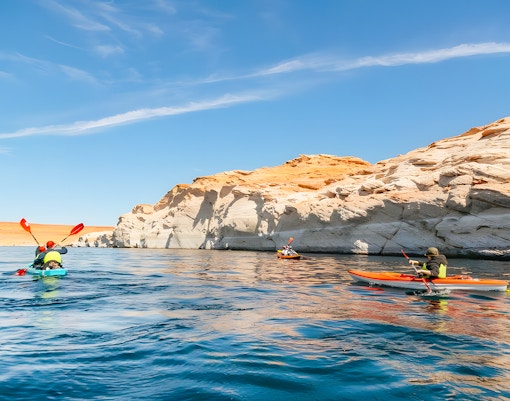 Kayakers paddling on Lake Powell near Antelope Canyon's sandstone cliffs.