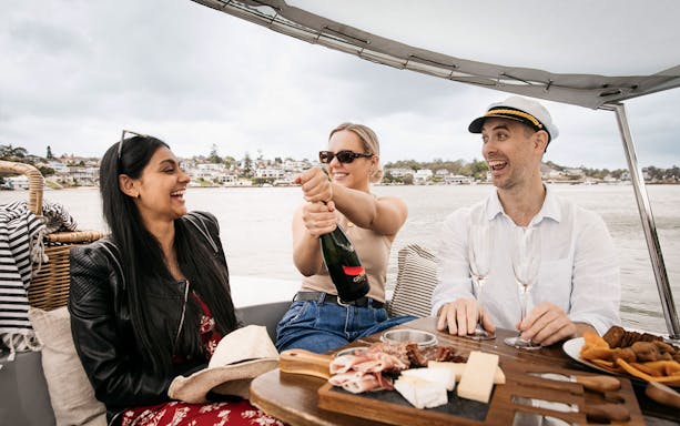 Friends enjoying a picnic with champagne on a self-drive electric boat in Sydney.