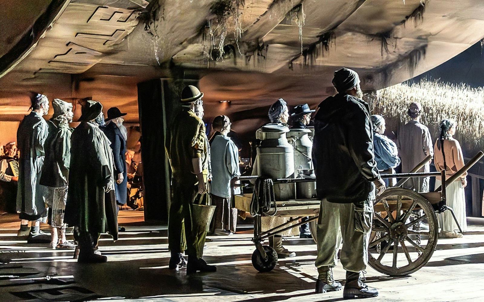 Actors on stage performing a scene from "Fiddler on the Roof" with a cart and milk cans.