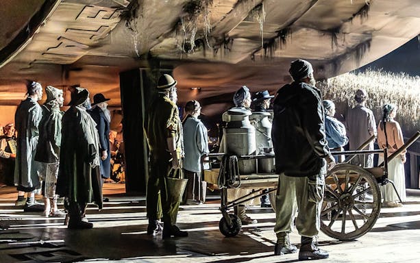 Actors on stage performing a scene from "Fiddler on the Roof" with a cart and milk cans.