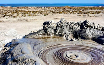 Mud volcano in Gobustan National Park with distant view of Baku, Azerbaijan.