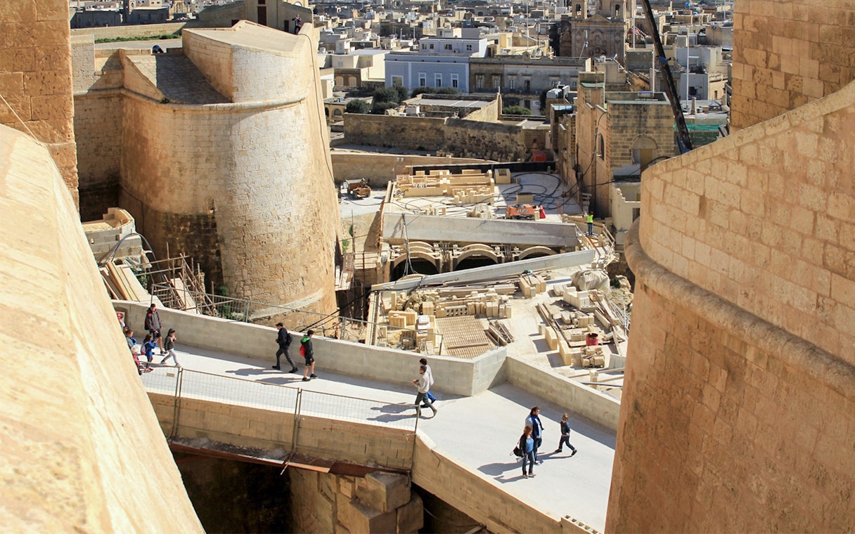 Visitors walking along the historic walls of Gozo, Malta, with cityscape in the background.