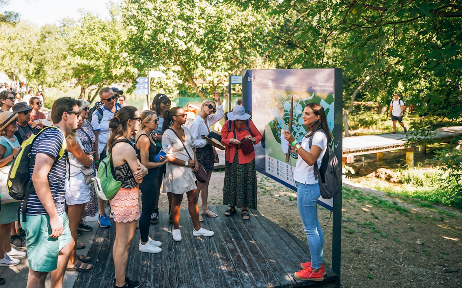 Tour group listening to a guide at Krka National Park, Croatia, near a map display.