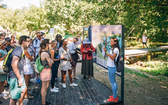 Tour group listening to a guide at Krka National Park, Croatia, near a map display.