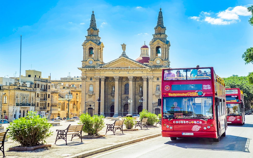 Hop-on hop-off bus in front of a historic church in Malta.