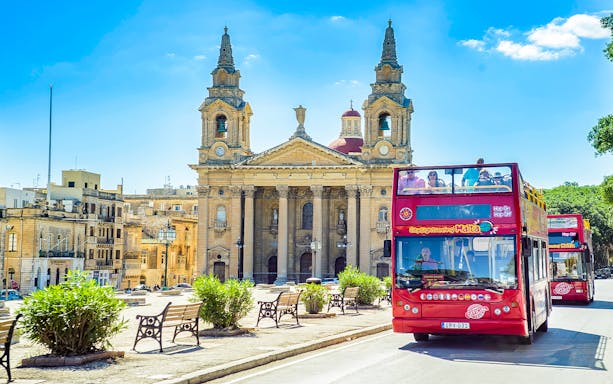 Hop-on hop-off bus in front of a historic church in Malta.