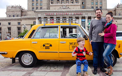 Family posing with yellow Fiat 125p taxi in front of Palace of Culture and Science, Warsaw.