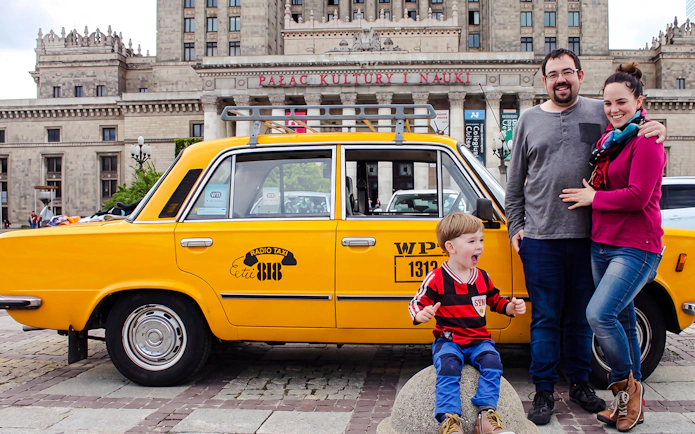 Family posing with yellow Fiat 125p taxi in front of Palace of Culture and Science, Warsaw.