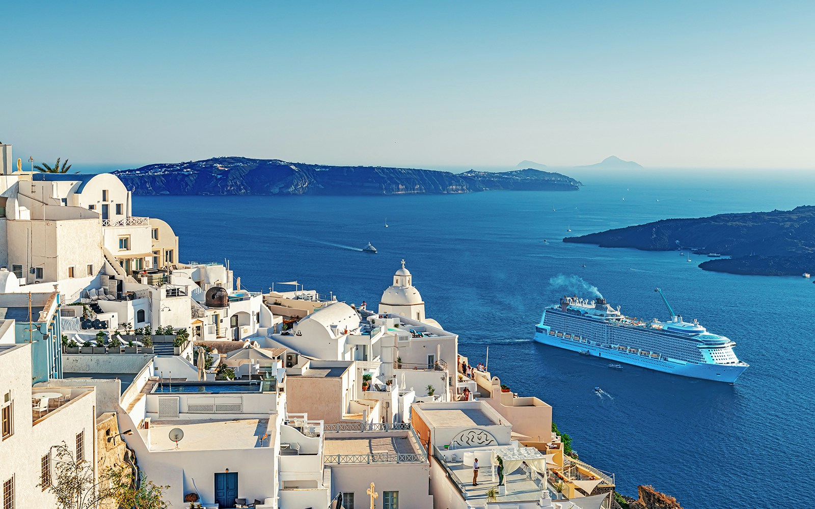 Cruise ship sailing near Santorini's white buildings and blue sea, Greece.