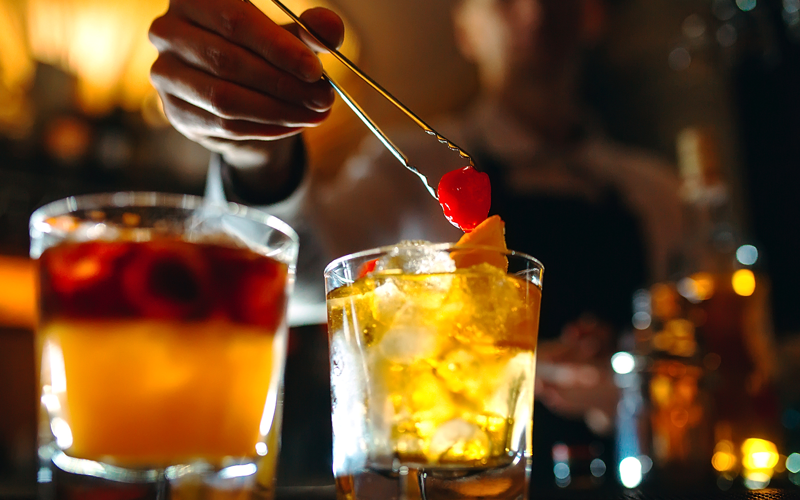 Bartender garnishing cocktails with cherries at a bar.
