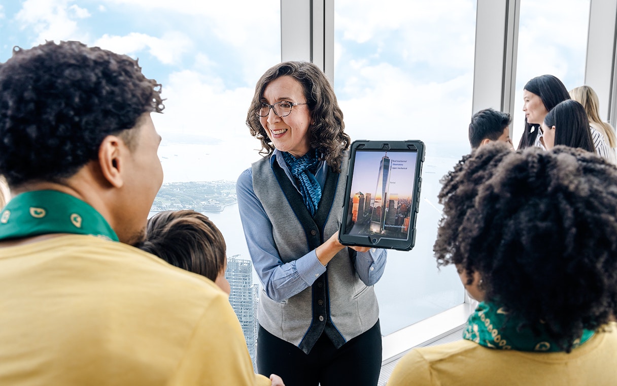 Guide showing One World Observatory view on tablet to visitors.