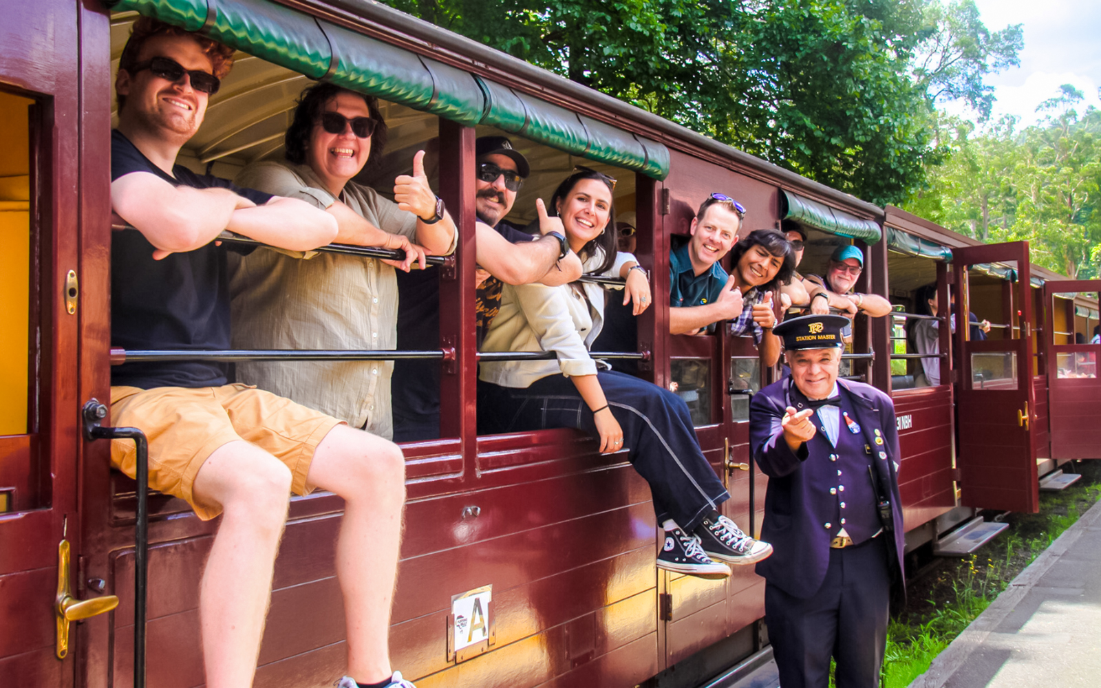 Friends and conductor on Puffing Billy steam train in open-sided carriage, Australia.