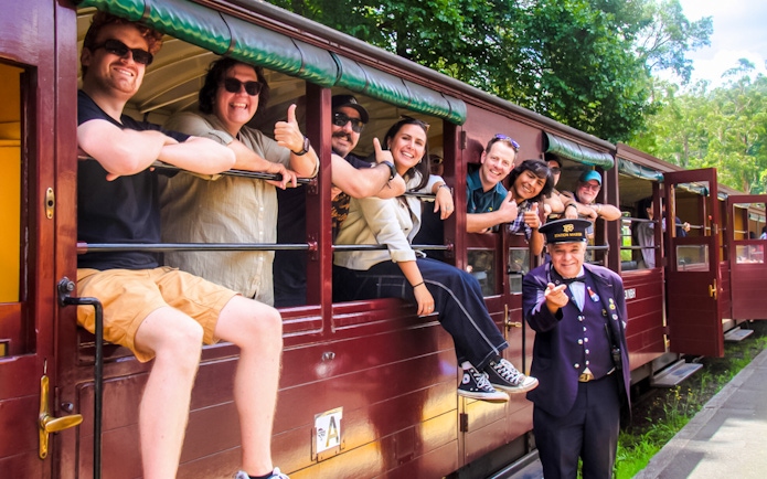 Friends and conductor on Puffing Billy steam train in open-sided carriage, Australia.