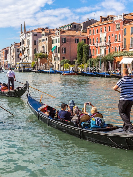 Gondolas navigating the Grand Canal in Venice, Italy with historic buildings in the background.