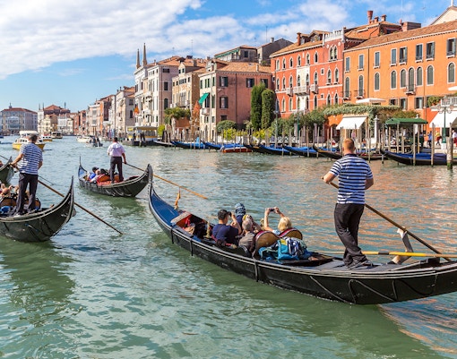 Gondolas on a canal in Venice, Italy, with historic buildings in the background.