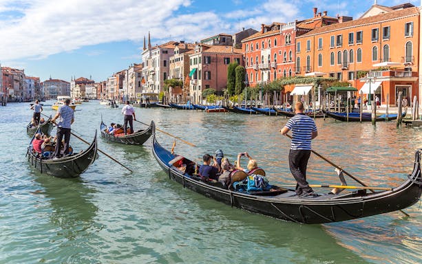 Gondolas navigating the Grand Canal in Venice, Italy with historic buildings in the background.