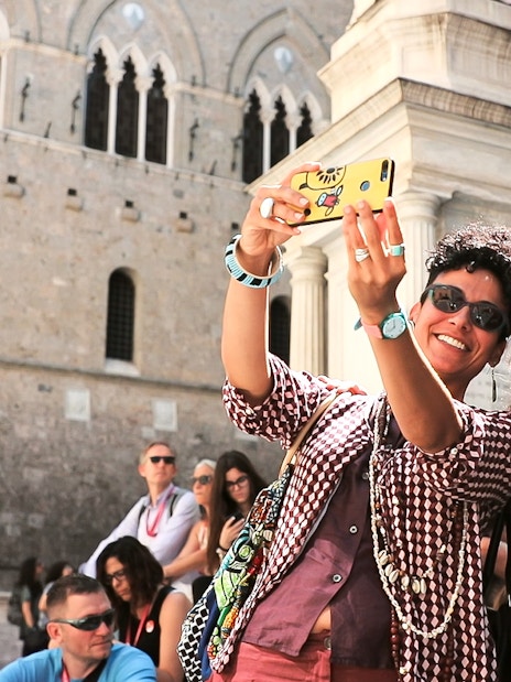 Tourists taking a selfie in front of historic architecture in San Gimignano, Italy.