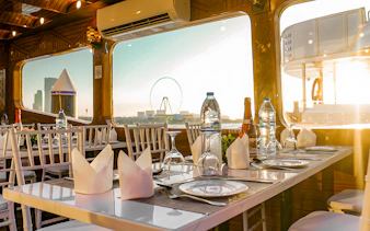 Dhow cruise dining setup with Dubai skyline and Ferris wheel view.