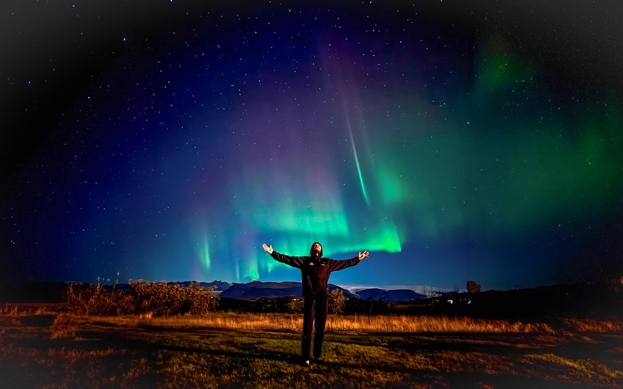 Person enjoying Northern Lights on off-road tour with hot chocolate.