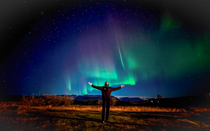 Person enjoying Northern Lights on off-road tour with hot chocolate.