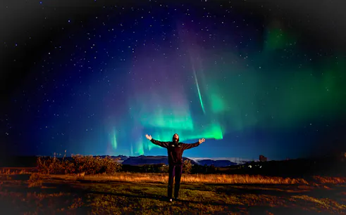 Person enjoying Northern Lights on off-road tour with hot chocolate.