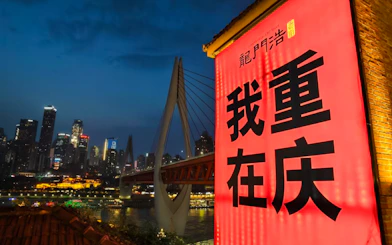 Chongqing skyline at night with illuminated bridge and Longmenhao sign.