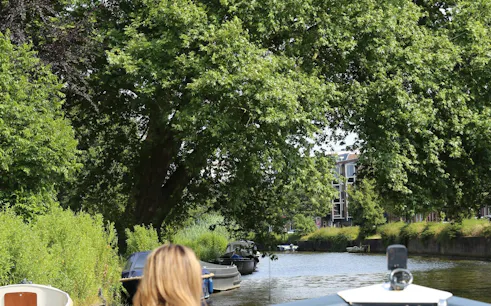 Open boat cruising through Haarlem canal with lush greenery and buildings in the background.