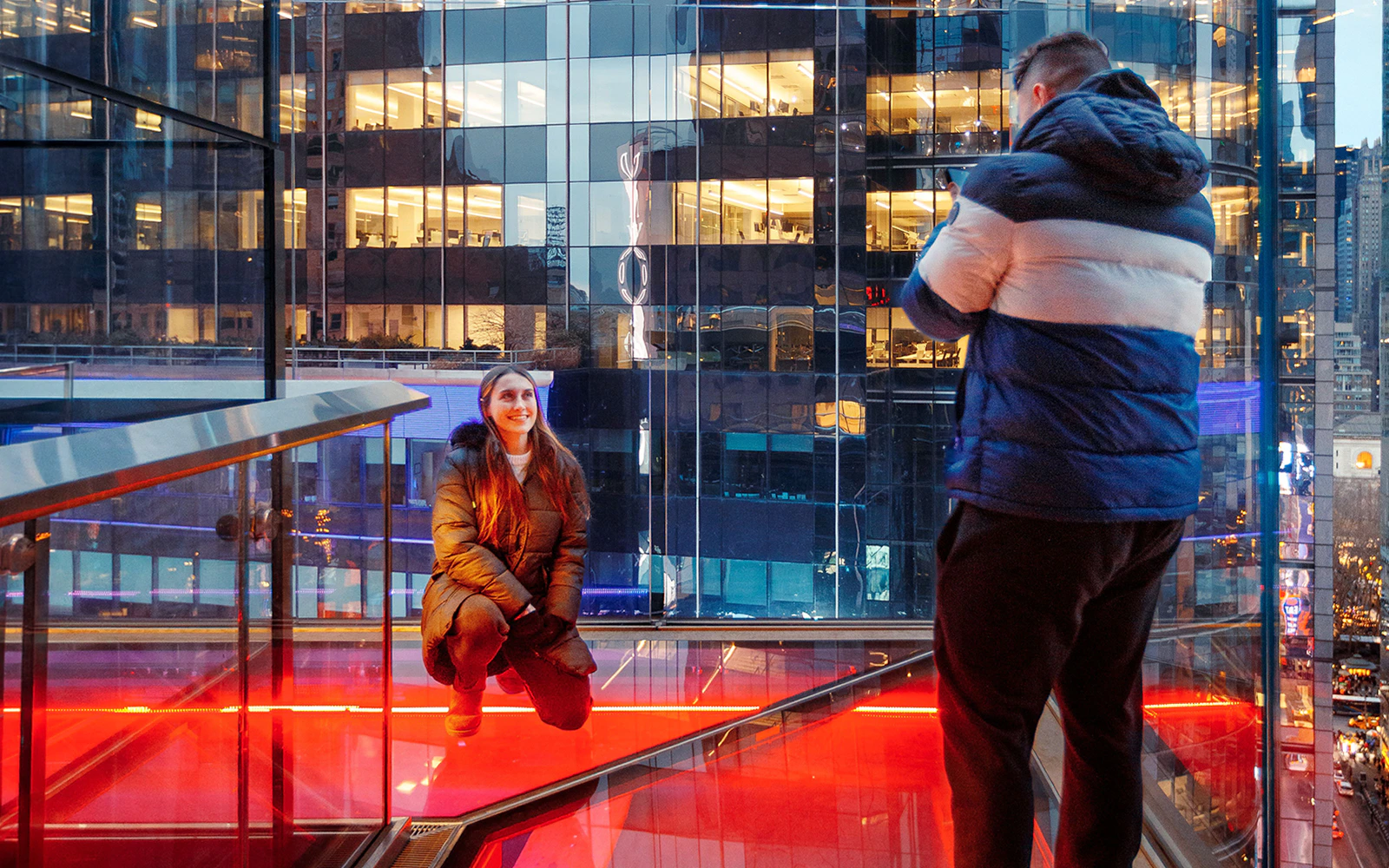 Person posing on One Times Square Skywalk with cityscape view in background.