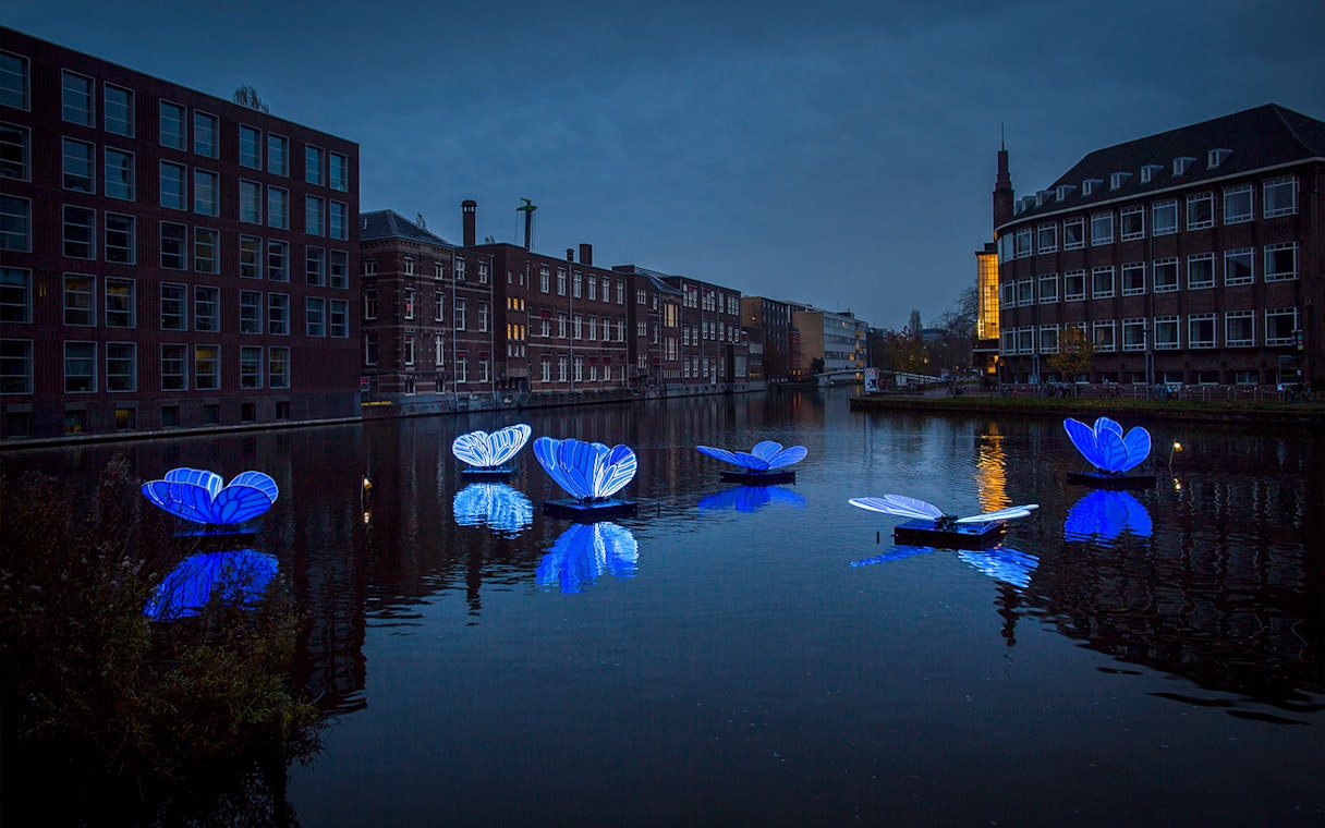 Floating blue light installations on an Amsterdam canal during the Light Festival.