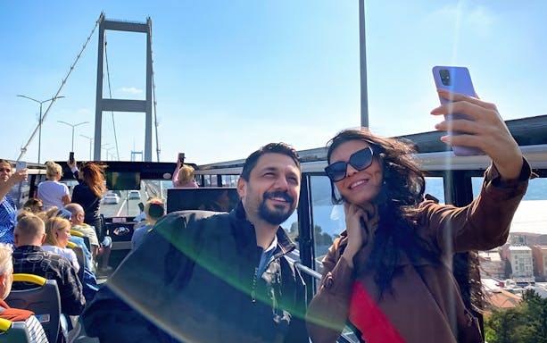 Tourists on Istanbul hop-on-hop-off bus taking selfies near Bosphorus Bridge.