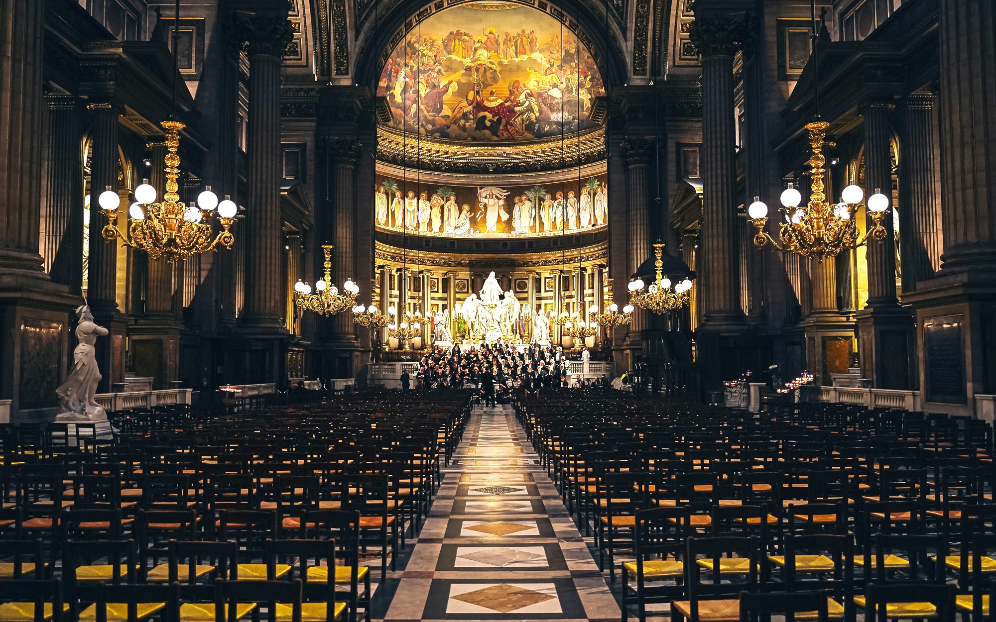 Orchestra performing in The Church of St Madeleine, Paris, France, with ornate interior and chandeliers.